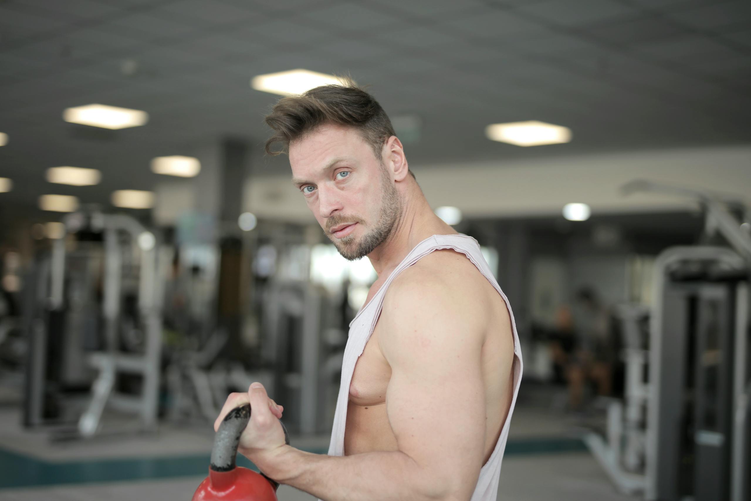 A muscular man in a gym environment working out with a kettlebell, showcasing strength and determination.